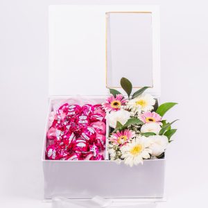 קופסה לבנה פתוחה עם שוקולדים ורודים וזר פרחים לבנים וורודים.