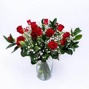 זר פרחים באגרטל זכוכית, עם ורדים אדומים, פרחי גיבסנית לבנים ועלי ירק, על רקע לבן.