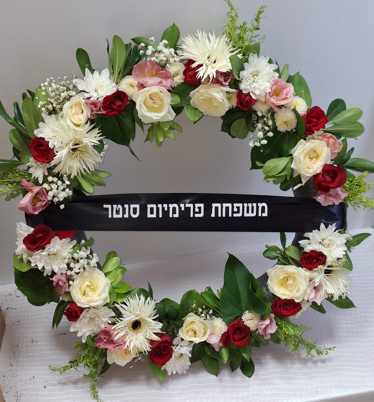 זר פרחים צבעוני עם סרט שחור ועליו כתוב "משפחת פרימיום נוסטר".
