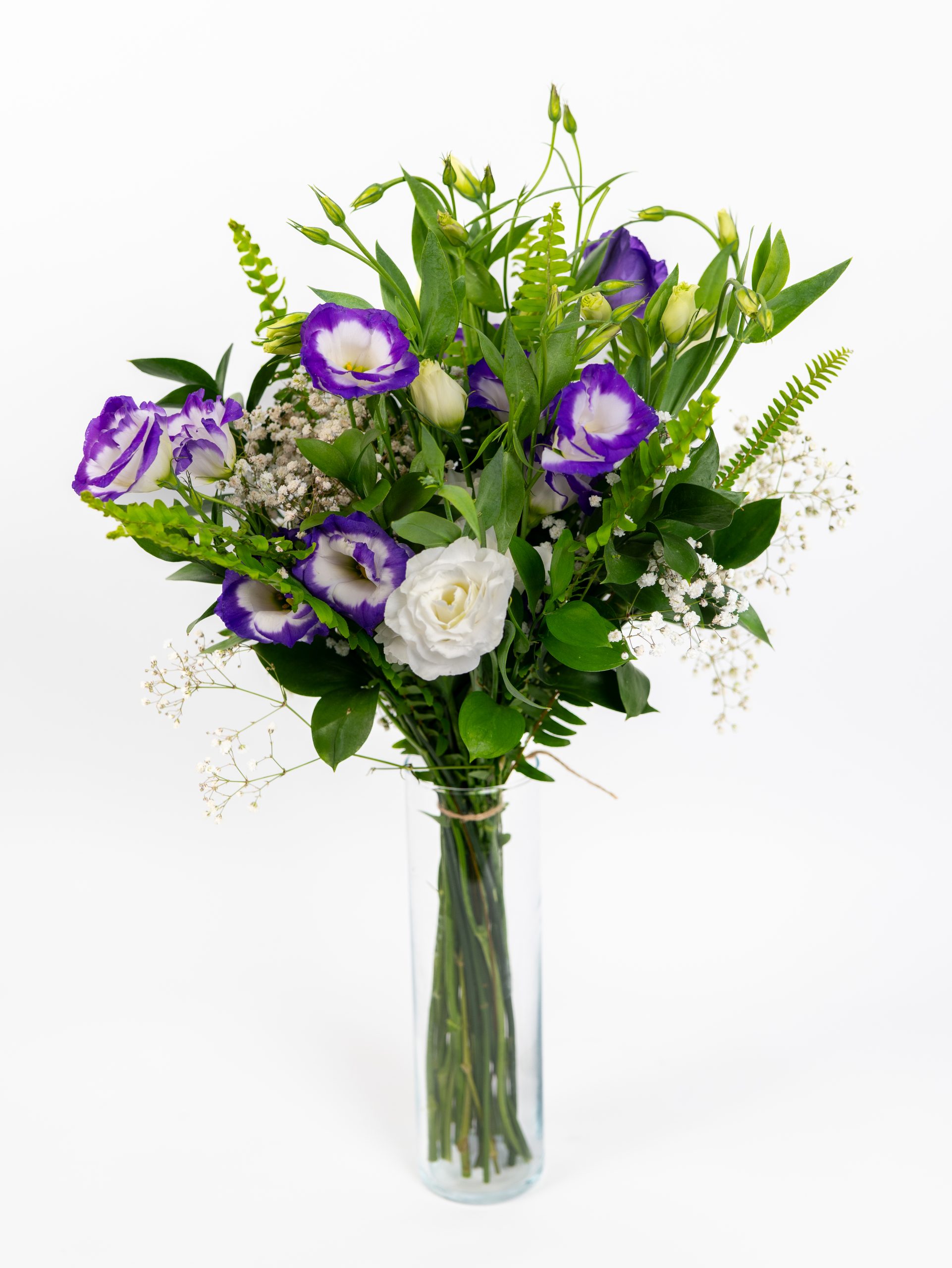 זר פרחים סגולים ולבנים עם עלים ירוקים ופרחי גבס קטנים מונח באגרטל זכוכית על רקע לבן.