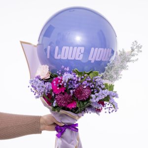 יד אוחזת בזר פרחים סגולים, ורודים ואדומים, המחובר לבלונים סגולים עם הכיתוב "אני אוהב אותך".