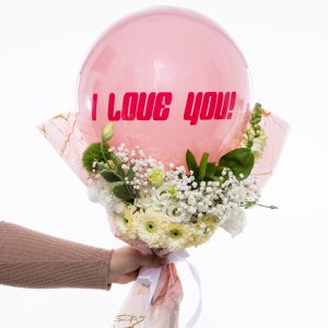 יד אוחזת בזר פרחים לבנים וורודים עם בלון ורוד עליו כתוב "אני אוהב אותך".