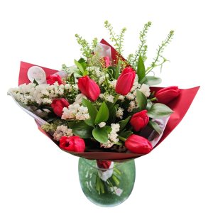 זר פרחים אדומים ולבנים עטוף בנייר אדום, מונח בתוך אגרטל זכוכית עגול.