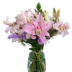 זר פרחים ורודים, לבנים וסגולים מונח באגרטל זכוכית שקוף מלא במים.