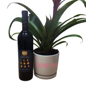 בקבוק יין אדום ליד עציץ עם פרח אדום, על העציץ כתוב "חג שמח" בכתב ורוד.