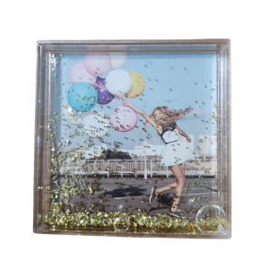 מסגרת תמונה שקופה עם נצנצים זהובים, בתוכה תמונה של אישה מחייכת רצה עם בלונים צבעוניים.