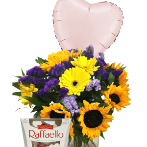 זר פרחים צהובים וסגולים באגרטל שקוף, בלון בצורת לב וקופסת שוקולד רפאלו.