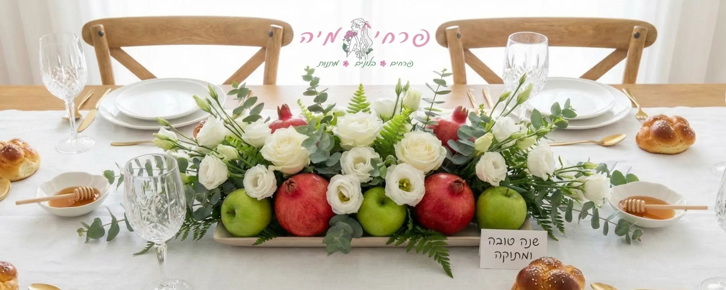 שולחן חג ערוך לראש השנה עם מפה לבנה, במרכזו סידור פרחים נמוך ומוארך המורכב מפרחים לבנים כמו ורדים וליזיאנטוס, בשילוב ענפי אקליפטוס ושרך רעננים. בין הפרחים משובצים רימונים אדומים שלמים ותפוחי עץ ירוקים. הסידור מונח על מגש שטוח ואינו מסתיר את הצלחות וכוסות היין שמסביב.