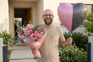 שליח עם חיוך מגיש זר פרחים מרהיב ובלון בכניסה לבית.