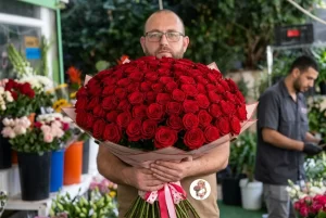 זר ורדים ענק ואדום הממלא את הפריים, מוחזק בשתי ידיים.