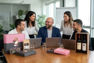 צוות עובדים במשרד מחייך סביב שולחן ישיבות שעליו מונחים מארזי שי יוקרתיים ויינות.